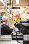 Senior female cashier helping customer at supermarket checkout — Stock Photo
