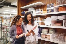 Happy women friends shopping for plates in home goods store — Stock Photo