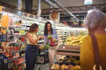Mujeres comprando fruta en la sección de productos de supermercado - foto de stock