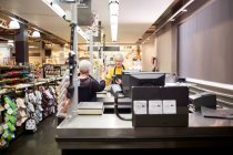 Caixa feminina sênior ajudando o cliente no checkout do supermercado — Fotografia de Stock