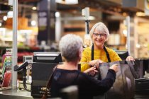 Amigável sênior feminino caixa ajudando cliente supermercado checkout — Fotografia de Stock