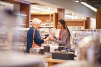 Mitarbeiterin hilft Seniorin beim Einkaufen im Haushaltswarengeschäft — Stockfoto