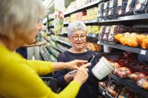 Femmes âgées avec téléphone intelligent épicerie au supermarché — Photo de stock