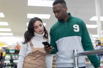 Female grocer helping male customer with smart phone in supermarket — Stock Photo