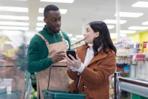 Männlicher Lebensmittelhändler hilft Kundin mit Smartphone im Supermarkt — Stockfoto