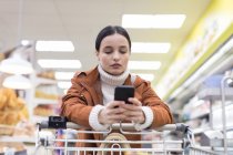 Молодая женщина со смартфонами в продуктовом магазине — стоковое фото