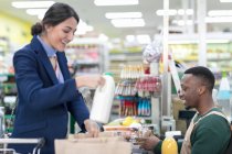 Male cashier helping female customer at checkout in supermarket — Stock Photo