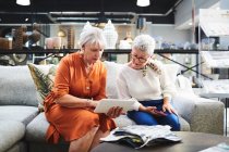 Seniorinnen mit digitalem Tablet betrachten Stoffmuster auf Sofa im Möbelhaus — Stockfoto