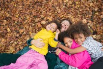 Portrait happy mother and children laying in autumn leaves — Stock Photo