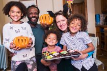 Retrato familia feliz con calabazas talladas y cupcakes de Halloween - foto de stock