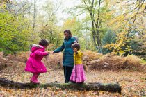 Mãe e filhas brincando no tronco caído em florestas de outono — Fotografia de Stock