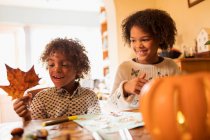 Happy brother and sister with autumn leaf doing crafts at table — Stock Photo
