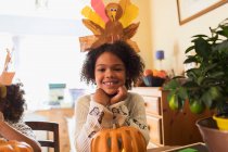 Portrait happy girl with turkey hat carving pumpkin at table — Stock Photo