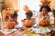 Brother and sisters with turkey hats carving pumpkins at table — Stock Photo