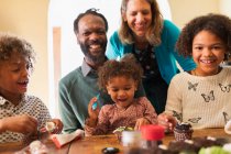 Retrato de familia multiétnica feliz decorando cupcakes en la mesa - foto de stock