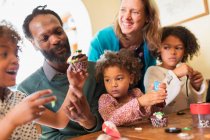 Happy multiethnic family decorating cupcakes at table — Stock Photo