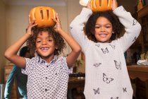 Portrait of happy brother and sister holding carved pumpkins overhead — Stock Photo