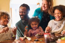 Feliz familia multiétnica decorando cupcakes en la mesa - foto de stock
