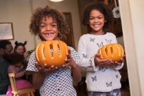 Portrait happy brother and sister holding carved pumpkins — Stock Photo