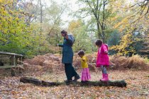Mother and daughters balancing on fallen log in autumn woods — Stock Photo