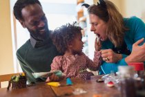 Glückliche multiethnische Familie dekoriert Halloween-Cupcakes am Tisch — Stockfoto