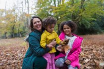 Ritratto felice madre e figlie che giocano in foglie autunnali nel bosco — Foto stock