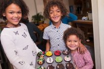 Retrato feliz hermano y hermanas con cupcakes de Halloween decorados - foto de stock