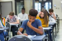 Сосредоточенный ученик старшей школы, сдающий экзамен за столом в классе — стоковое фото