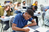 Estudante focado do ensino médio fazendo exame na mesa em sala de aula — Fotografia de Stock