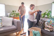 Mature couple folding laundry and sweeping living room — Stock Photo