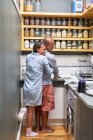 Feliz mujer cariñosa abrazando marido haciendo platos en la cocina. - foto de stock