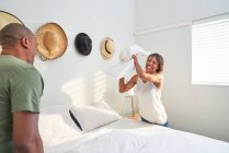 Playful couple making bed in bedroom — Stock Photo