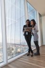 Lächelnde Geschäftsfrauen mit digitalem Tablet im Bürofenster eines Hochhauses — Stockfoto