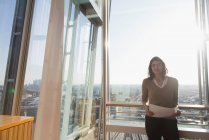 Portrait confident businesswoman at sunny highrise office window — Stock Photo
