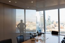 Silhouette businessman standing at urban highrise office window — Stock Photo