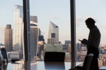 Silhouette businessman using smart phone at urban highrise window — Stock Photo