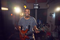 Портрет уверенного мужчины-музыканта, играющего на гитаре в студии звукозаписи — стоковое фото