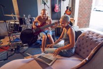 Smiling musicians with laptop and guitar in recording studio — Stock Photo