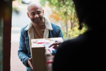 Доставка чоловік доставляє пакет жінці біля вхідних дверей — стокове фото