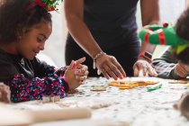 Mädchen dekoriert Weihnachtsplätzchen mit Familie am Tisch — Stockfoto