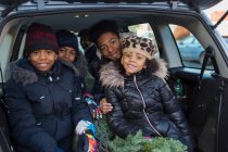 Retrato irmãos felizes e irmã com árvore de Natal na parte de trás do carro — Fotografia de Stock