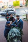 Ritratto felice famiglia che porta albero di Natale nel vialetto — Foto stock