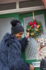 Feliz madre e hija colgando corona de Navidad en la puerta principal - foto de stock