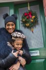 Retrato feliz madre e hija en la puerta principal con corona de Navidad - foto de stock