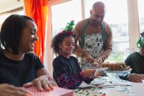 Щаслива сім'я, що обгортає різдвяні подарунки та листівки за столом — стокове фото
