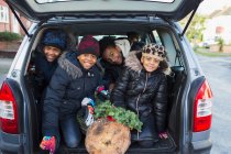 Retrato irmãos felizes e irmã com árvore de Natal na parte de trás do carro — Fotografia de Stock