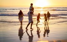 Família vagando no surf na idílica praia oceânica ao pôr-do-sol — Fotografia de Stock