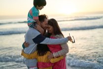 Glückliche, liebevolle Familie, die sich bei Sonnenuntergang am Strand am Meer umarmt — Stockfoto