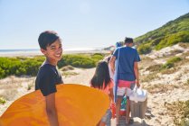Retrato menino feliz carregando bodyboard na praia ensolarada com a família — Fotografia de Stock
