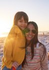 Portrait happy mother and daughter on sunny beach at sunset — Stock Photo